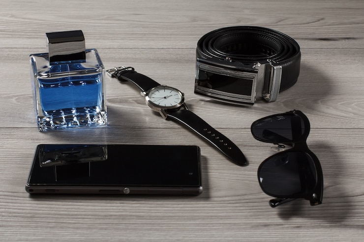 Photo parfum d'homme, montre avec un bracelet en cuir, ceinture en cuir avec boucle en métal, vente de téléphone, lunettes de soleil noires sur fond de bois gris