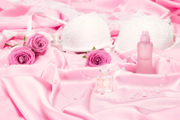 Parfums aux roses et sous-vêtements féminins sur soie rose. Choix de parfum pour concept de rendez-vous romantique