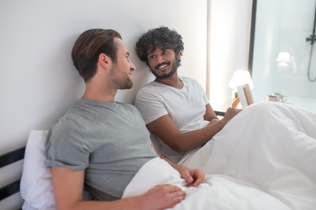 Photo parle avant de dormir. couple d'hommes au lit parlant et ayant l'air satisfait