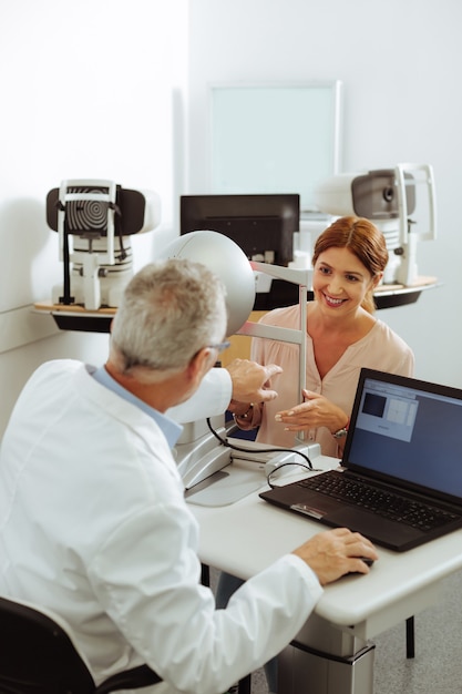 Parler au docteur. Belle patiente joyeuse d'une clinique ophtalmologique privée souriant tout en parlant au médecin