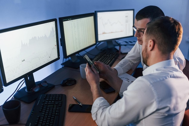 Parler entre eux Deux négociants en bourse travaillant au bureau avec la technologie d'échange