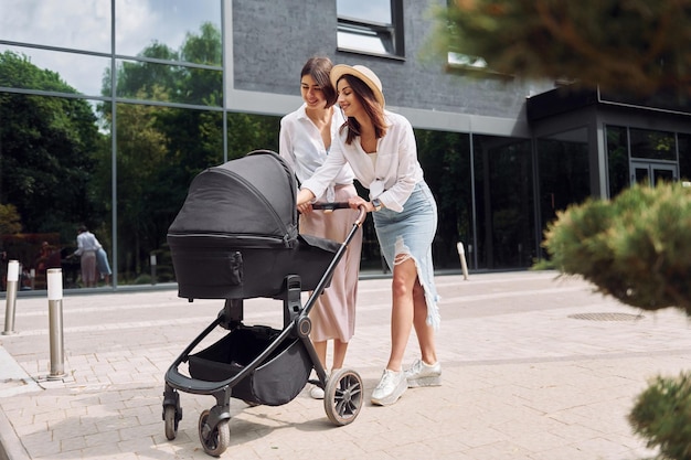 Parler et s'amuser Deux amies se promener avec un landau à l'extérieur