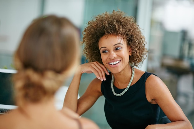 Le partage d'une excellente relation de travail Photo de deux collègues souriants parlant ensemble assis dans un bureau moderne