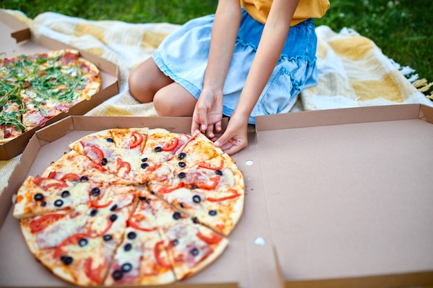 Partage de pizza, mains de petite fille prenant un morceau de pizza dans une boîte en plein air, pique-nique familial, manger des pizzas pour le dîner, livraison de restauration rapide.