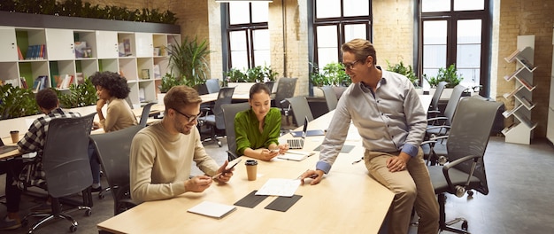 Partageant de nouvelles idées trois jeunes collègues assis au bureau dans l'espace de coworking moderne