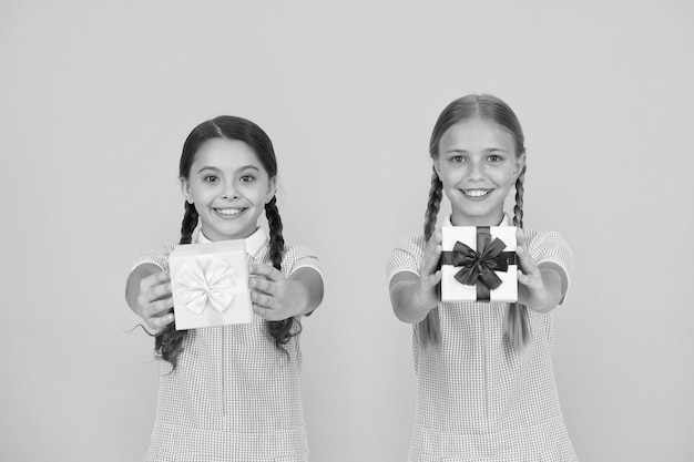 Partager le bonheur Célébration des fêtes Partager des cadeaux Filles ouvrant des cadeaux fond jaune Camarades de classe donnant des coffrets cadeaux Programme éducatif pour les enfants surdoués Vacances scolaires Générosité de l'éducation