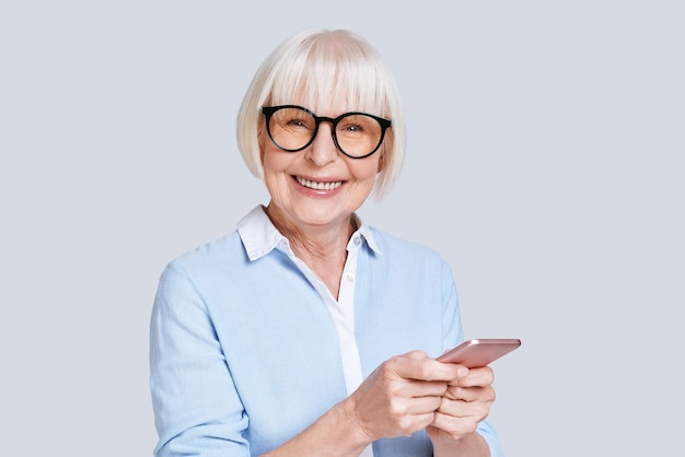 Partager de nouvelles idées. Belle femme âgée utilisant son téléphone intelligent et souriant