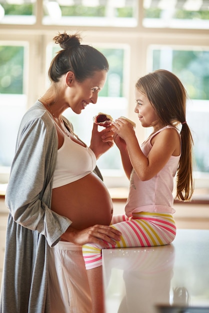 Partager quelques friandises ensemble Photo d'une femme enceinte et d'une jeune fille mangeant des cupcakes ensemble