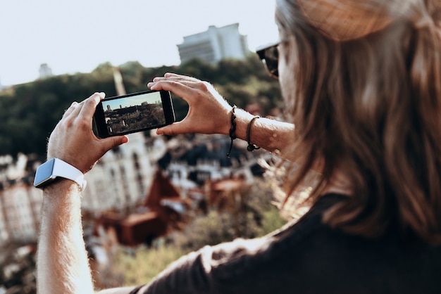 partager la vue. vue arrière du jeune homme photographiant la vue à l'aide d'un téléphone intelligent