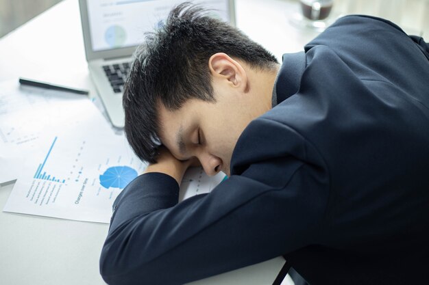 Les partenaires commerciaux conçoivent un jeune homme d'affaires dormant sur un bureau avec un ordinateur portable et un document après avoir travaillé longtemps.