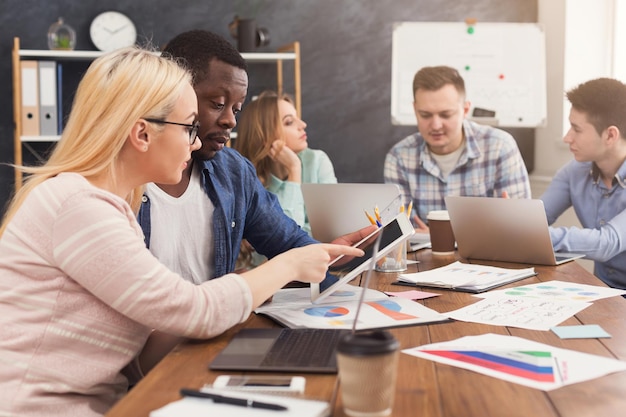 Partenaires commerciaux sérieux travaillant dans un bureau moderne. Deux collègues multiethniques inquiets discutant d'un nouveau projet tout en travaillant sur un ordinateur portable, un espace de copie