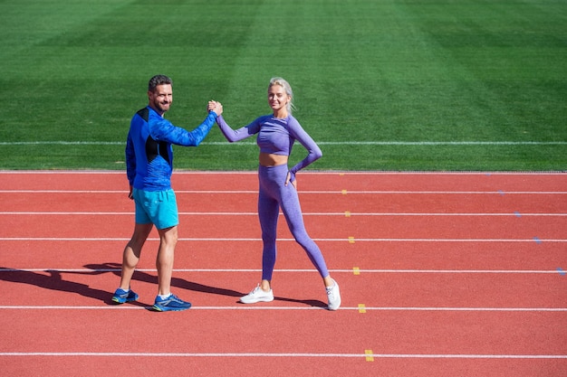 les partenaires de fitness du couple sportif célèbrent la victoire de l'équipe avec un geste de poignée de main après l'exercice ou la compétition de bras de fer sur l'arène de la piste de course du stade en plein air, le succès sportif.