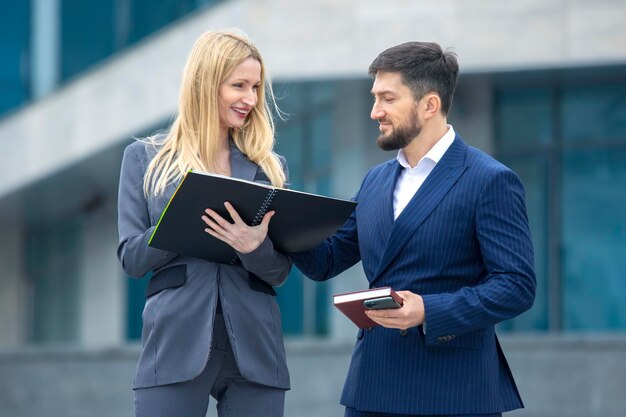 Partenaires d'hommes d'affaires prospères sur le fond d'un bâtiment d'entreprise avec des documents dans leurs mains discutant de projets d'entreprise