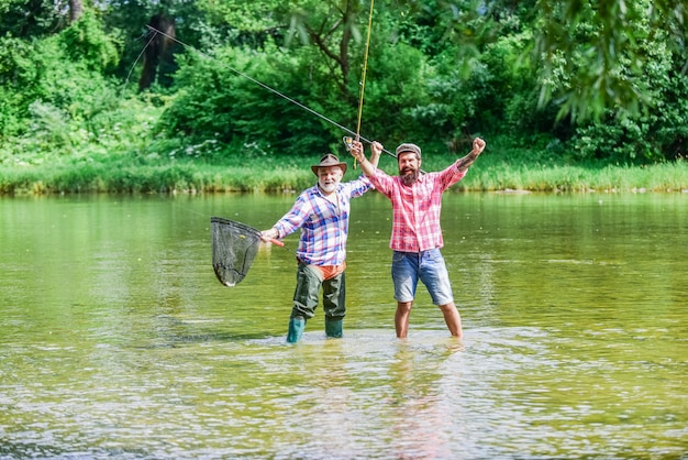 Partenaires loisirs et loisirs en plein air deux pêcheurs heureux avec canne à pêche et filet passe-temps et activité sportive appâts à truite père et fils aventures de pêche pêche au gros amitié masculine