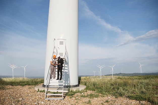 Partenaires multiraciaux debout près d'un moulin à vent et utilisant une tablette