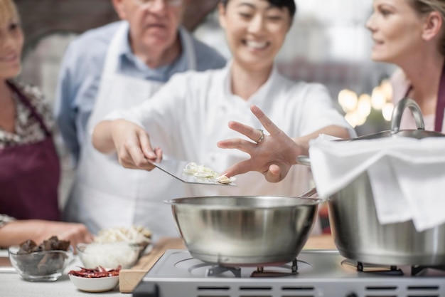 Des participants à un cours de cuisine regardant une femme cuisiner.