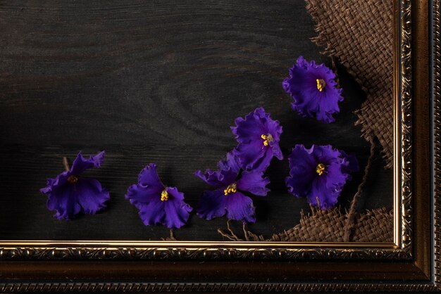 Une partie d'un beau cadre contient un tissu rugueux sur un fond en bois et des fleurs violettes