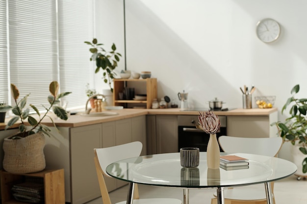 Partie d'une cuisine spacieuse avec une table en verre ronde avec des vases et des blocs-notes