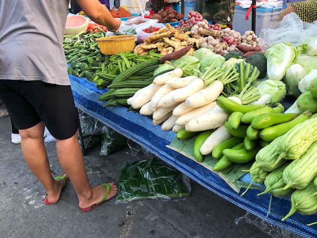 Une partie du corps de la femme devant un étal de légumes au marché frais.