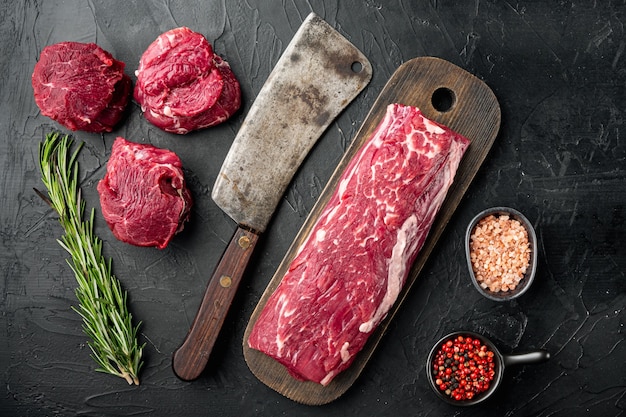 Partie gastronomique du filet de boeuf marbré frais cru, avec de vieux couteau couperet de boucher, sur table en pierre noire, vue de dessus à plat