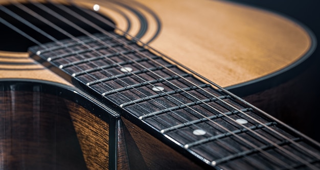 Partie d'une guitare acoustique, manche de guitare avec cordes sur fond noir.