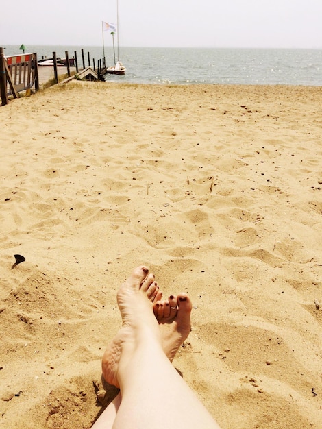 Photo la partie inférieure de la femme assise sur la plage contre le ciel