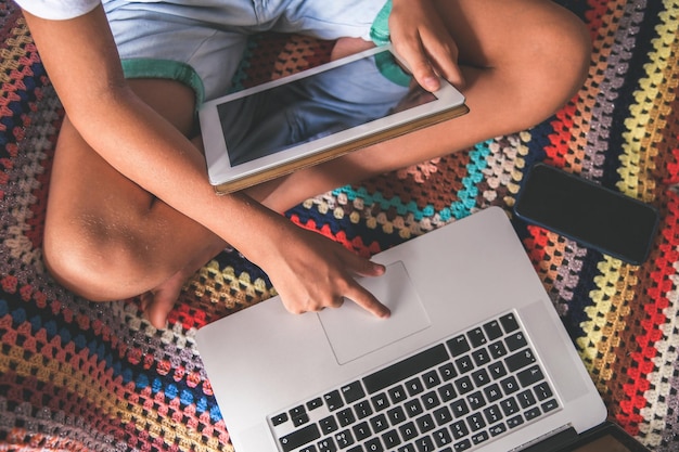 Photo la partie inférieure d'un garçon utilisant une tablette numérique et un ordinateur portable à la maison