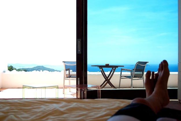Photo la partie inférieure de l'homme allongé sur le lit avec la mer et le ciel vus par la fenêtre