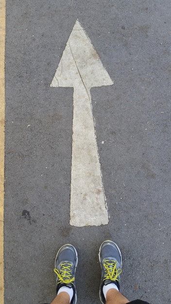 La partie inférieure de l'homme debout par le symbole de la flèche sur la route