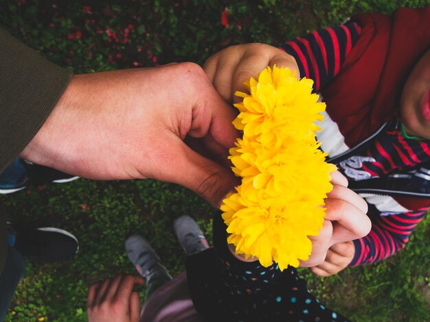 Photo la partie inférieure de l'homme donnant des marigolds jaunes aux enfants debout sur le champ