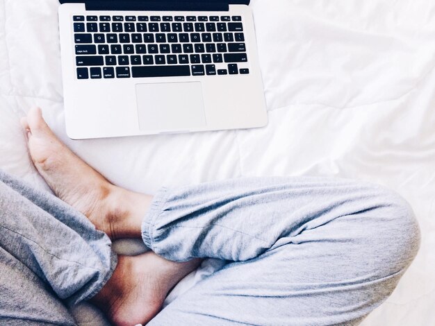 La partie inférieure de l'homme utilisant l'ordinateur portable dans le lit