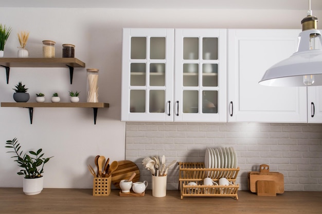 Une partie de l'intérieur d'une cuisine moderne blanche avec des armoires en verre dépoli, un mur en brique blanche et un comptoir en bois. équipement de cuisine.