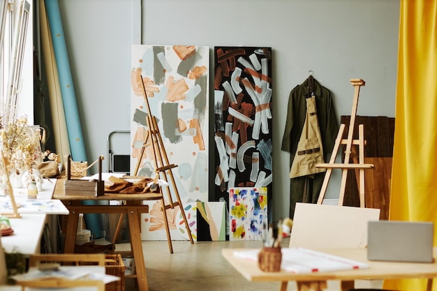 Photo une partie de spacieux studio d'arts avec des chevalets en bois peintures sur toiles vêtements de travail accroché au mur un