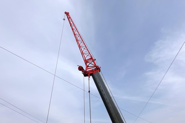 Partie supérieure rouge de la grande flèche de la grue de construction et de nombreux câbles métalliques tirés dans le ciel bleu