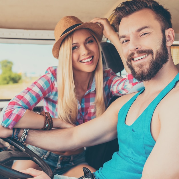 Partir en week-end. Heureux jeune couple souriant à la caméra alors qu'il était assis à l'intérieur de la fourgonnette