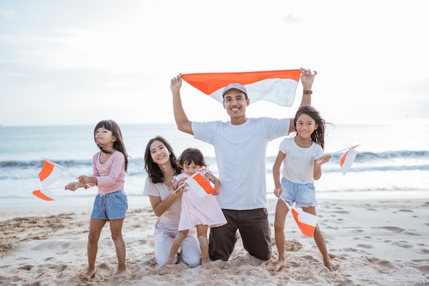 Partisan de la famille indonésienne enthousiaste avec le drapeau indonésien sur la plage ensemble