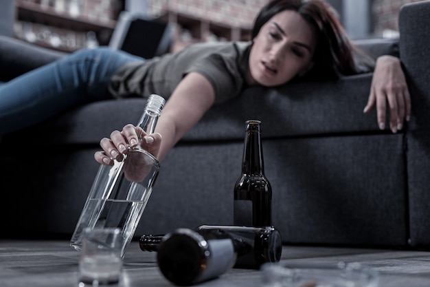 Pas assez. Mise au point sélective d'une bouteille d'alcool prise par une femme malheureuse ivre en position couchée sur le canapé