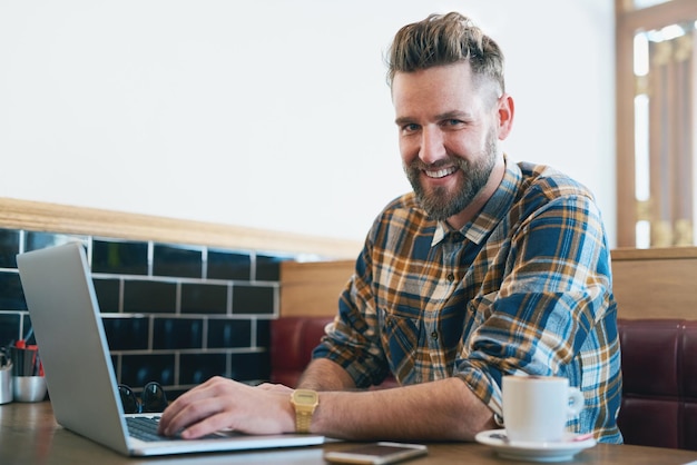 Pas de café pas de travail Portrait d'un jeune homme utilisant son ordinateur portable assis dans un café