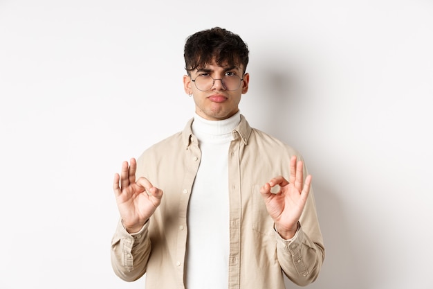 Photo pas mal. jeune homme satisfait montrant des gestes corrects et hochant la tête en signe d'approbation, louant le bon travail, satisfait des résultats, debout sur fond blanc