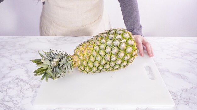 Pas à pas. Couper l'ananas sur une planche à découper blanche.