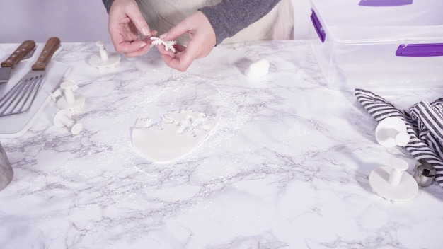 Pas à pas. Découper des flocons de neige avec des emporte-pièces en fondant blanc sur un comptoir en marbre.