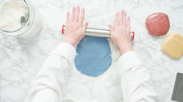 Pas à pas. Mise à plat. Étaler la pâte avec un rouleau à pâtisserie pour cuire des biscuits au sucre rouges, blancs et bleus.