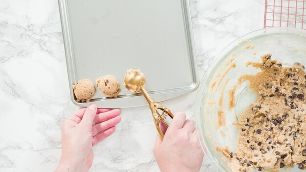 Photo pas à pas. mise à plat. ramasser des biscuits aux pépites de chocolat faits maison avec une cuillère à pâte en métal sur la plaque à pâtisserie.