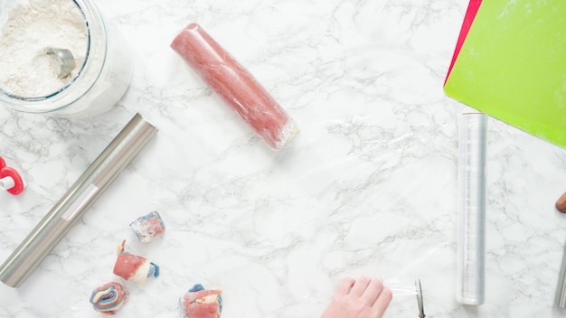 Pas à pas. Mise à plat. Étaler la pâte avec un rouleau à pâtisserie pour cuire des biscuits au sucre rouges, blancs et bleus.