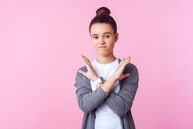 Pas question, fini. Portrait d'une adolescente brune mécontente avec une coiffure en chignon dans des vêtements décontractés se croisant les mains, montrant le geste de déni du signe stop x. studio d'intérieur tourné isolé sur fond rose