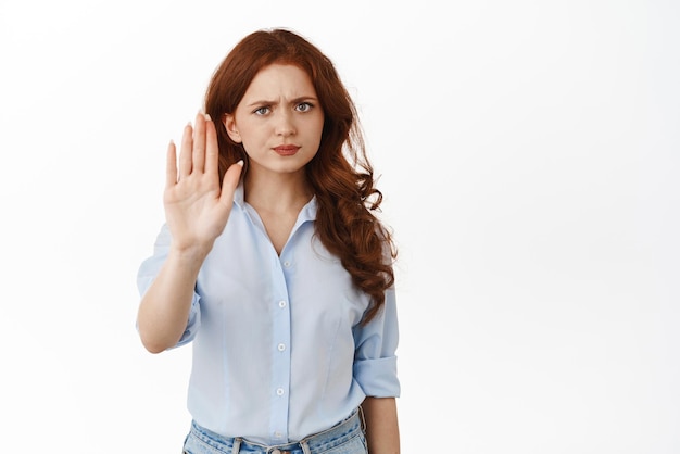 Pas de sérieux fronçant les sourcils femme rousse montrer arrêter interdire le geste garder vos distances rester à l'écart du signe debout mécontent sur fond blanc