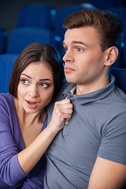 Pas si effrayant. Vue latérale d'un jeune couple regardant un film au cinéma pendant qu'une femme se lie à son petit ami