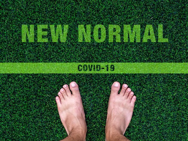 Passage au nouveau concept normal. Pieds nus sur l'herbe verte artificielle avec texte "New Normal" et ligne, après le concept de situation de pandémie de coronavirus COVID-19.