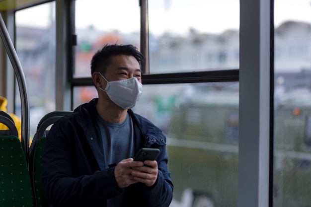 Un passager asiatique portant un masque médical de protection sur le visage écrit et lit anxieusement les nouvelles d'un téléphone portable, un homme parcourt la ville en bus des transports en commun