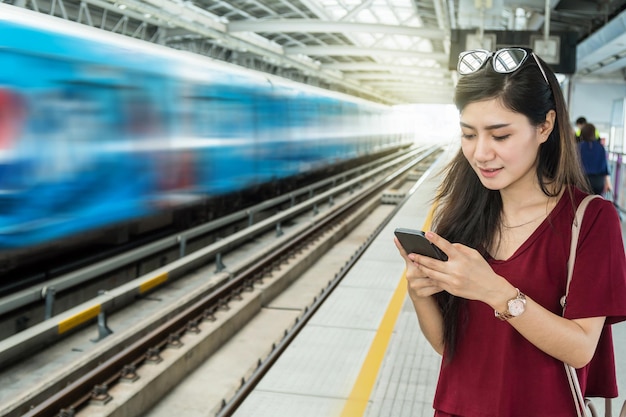 Passager femme asiatique avec costume décontracté à l&#39;aide du réseau social via téléphone mobile intelligent